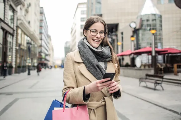 Shopper Using Flexible Payments Smiling shopper holding a smartphone and shopping bags after paying with Buy Now, Pay Later