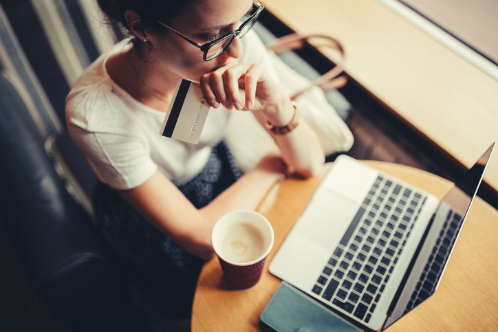 Woman in a cafe on laptop, holding credit card. worried about chargebacks