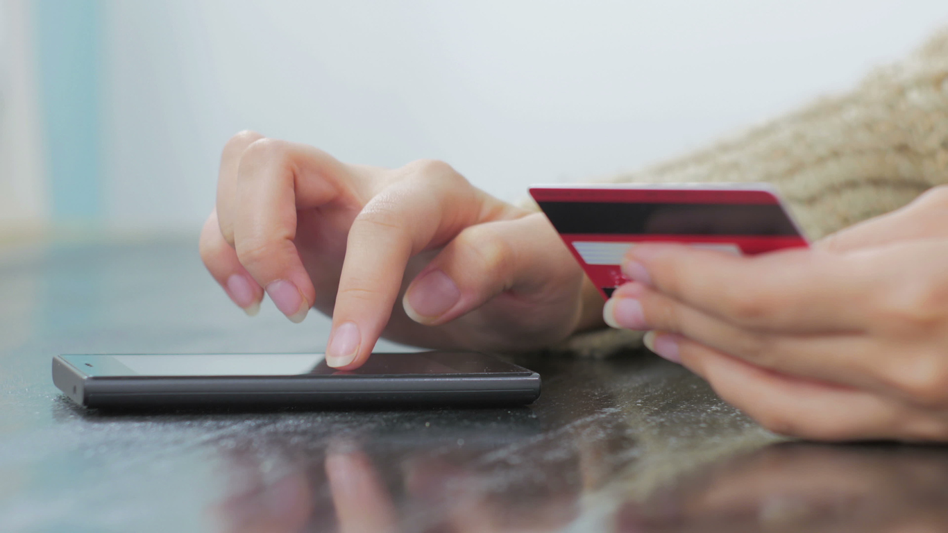 Young woman buying goods from the internet and entering number security code from credit card on smartphone. Mobile payment processors concept